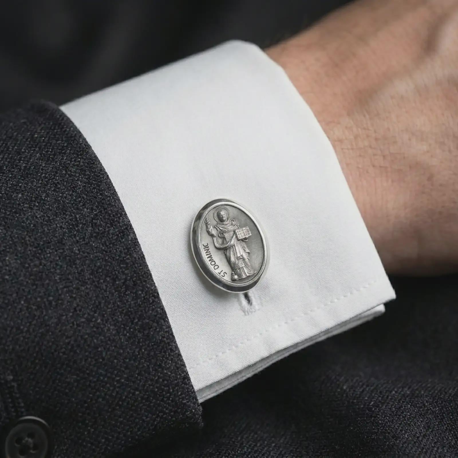 An oxidized St Dominic cufflink is worn on a white shirt cuff in a close-up lifestyle shot, styled with a dark suit as a meaningful Catholic accessory.