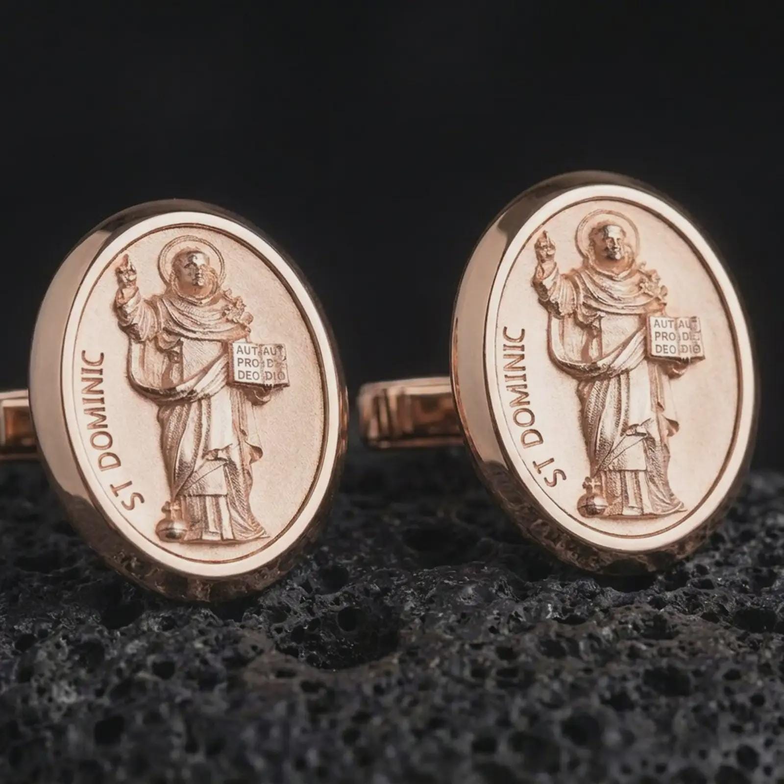 Rose gold plated St Dominic cufflinks are photographed on porous volcanic rock in a close-up studio composition with refined luxury lighting and religious detail.