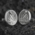 Load image into Gallery viewer, An oxidized Pensive Christ cufflink pair rests on dark volcanic rock in a macro studio close-up, showing a seated Jesus relief inside oval frames.
