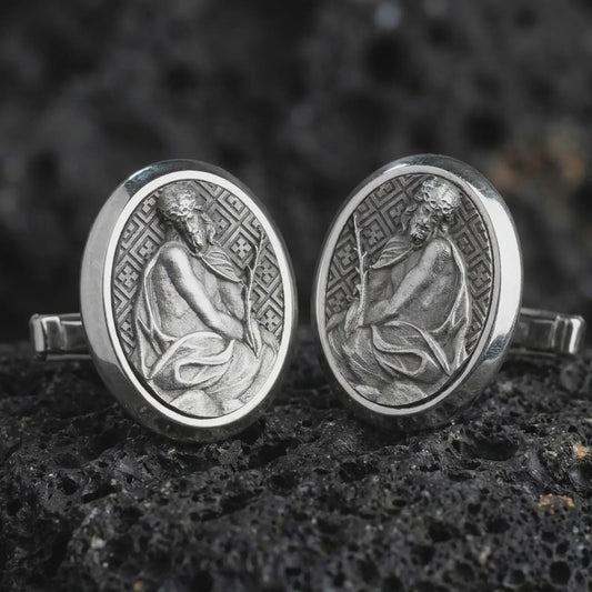 An oxidized Pensive Christ cufflink pair rests on dark volcanic rock in a macro studio close-up, showing a seated Jesus relief inside oval frames.