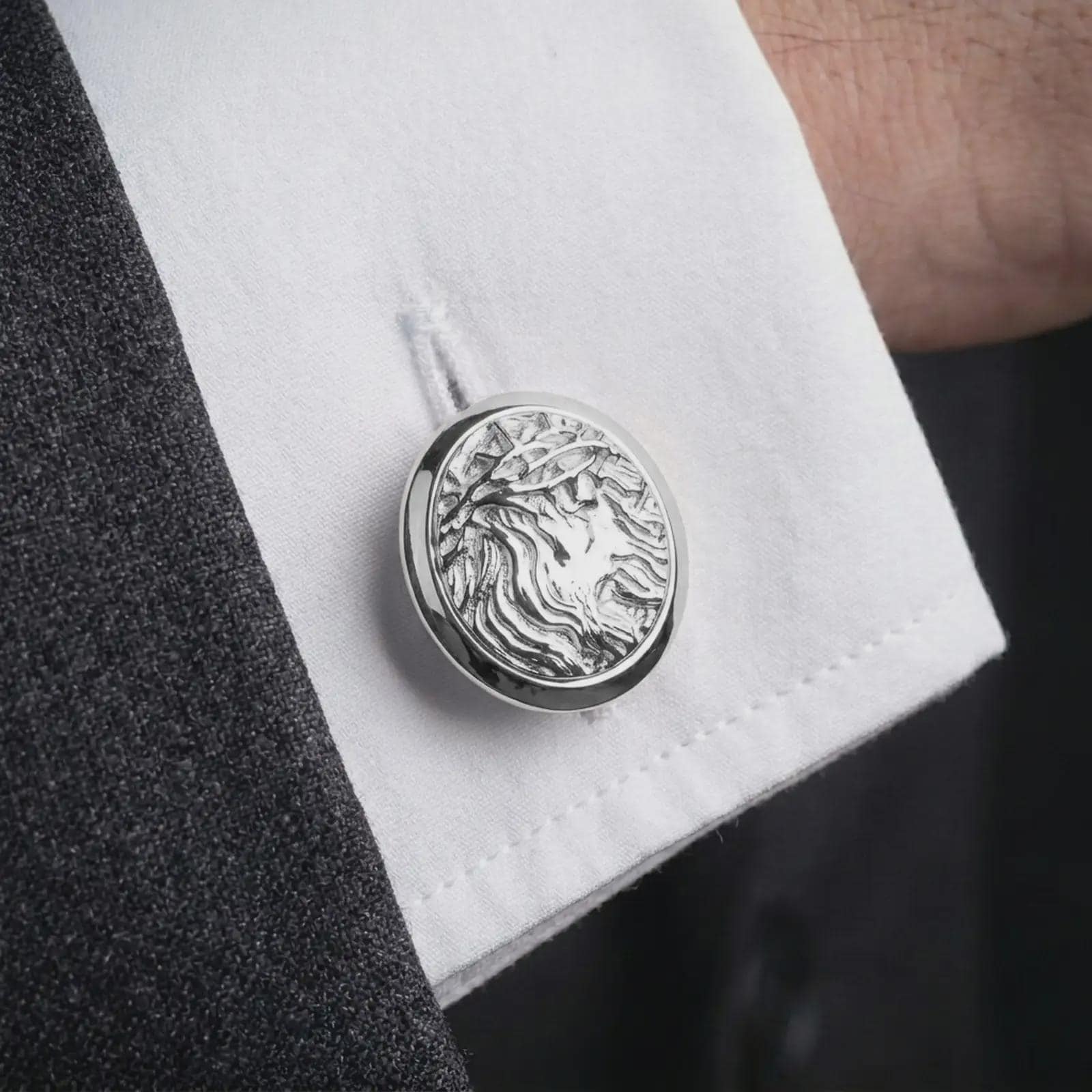 A polished silver Jesus Crown of Thorns cufflink is worn on a shirt cuff in a premium close-up lifestyle image, showing the Christ portrait clearly.
