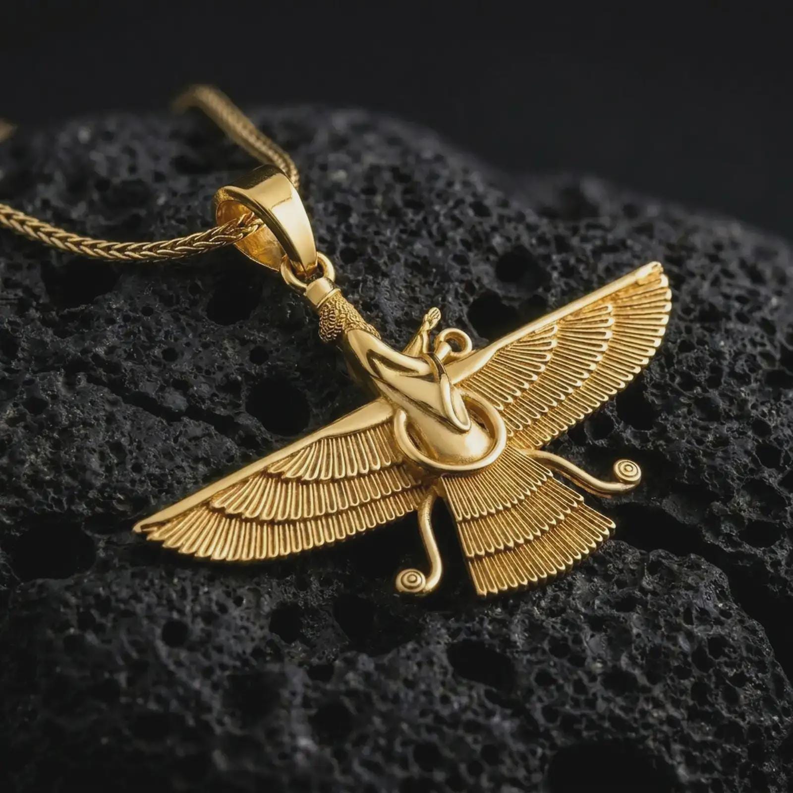 Gold plated Faravahar pendant necklace on textured volcanic rock, premium close-up studio composition emphasizing the ancient Persian wings, central figure, and spiritual amulet design.