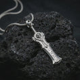 Load image into Gallery viewer, A polished silver demon slayer sword pendant is displayed on black volcanic rock in a premium macro studio close-up with sharp sculpted edges and an ornate guard.

