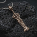 Load image into Gallery viewer, An Bronze demon slayer sword pendant rests on dark volcanic rock in a macro studio close-up, showing a fierce fantasy blade with rune-like details.
