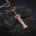Load image into Gallery viewer, A rose gold plated demon slayer sword pendant is photographed on porous volcanic rock in a close-up studio composition with bold luxury lighting and detailed blade texture.
