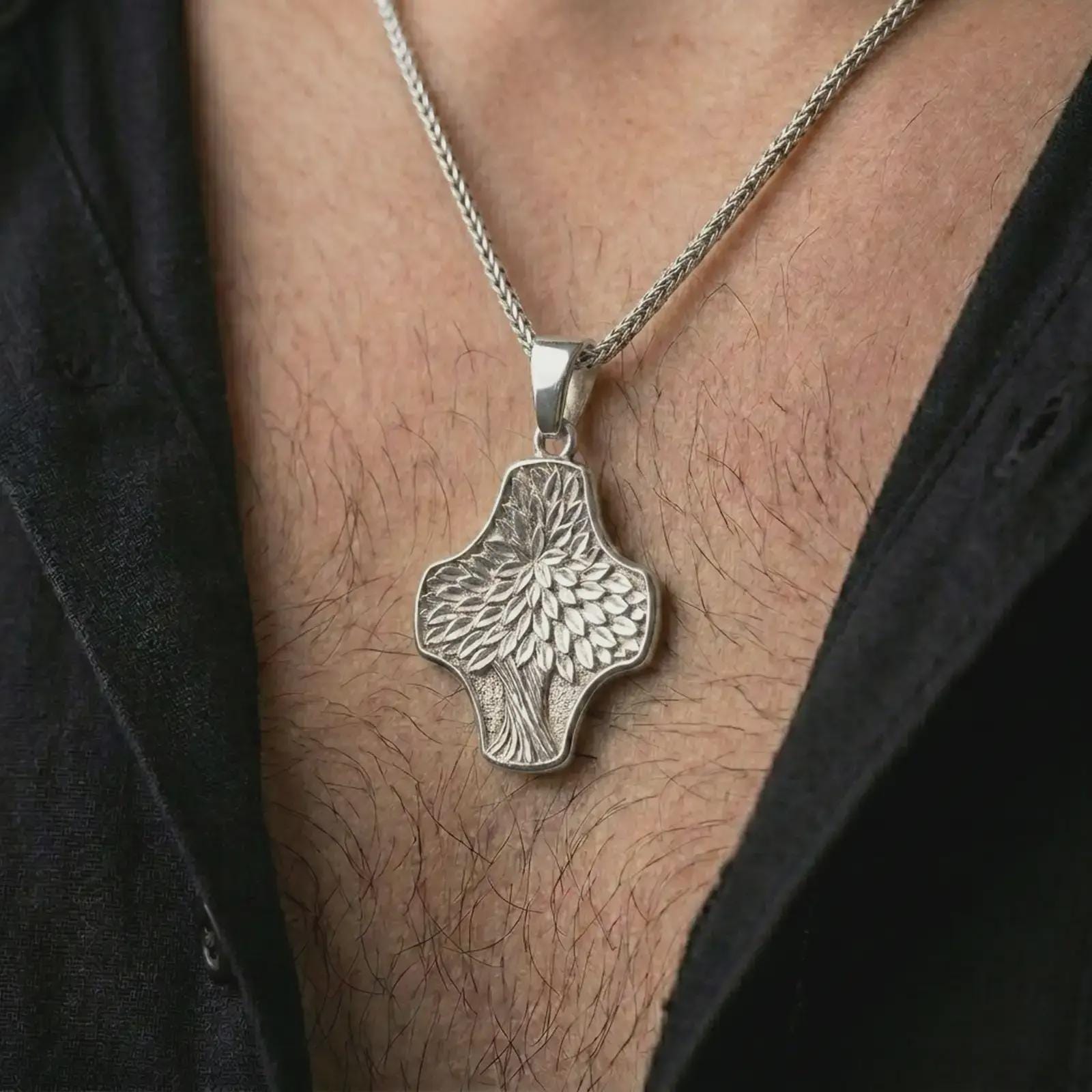 A polished silver Tree of Life cross pendant is worn on the neck in a premium close-up lifestyle image, showing the organic leaf pattern clearly.