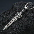 Load image into Gallery viewer, A polished silver fantasy sword pendant is displayed on black volcanic rock in a premium macro studio close-up with sharp blade lines and an ornate guard.
