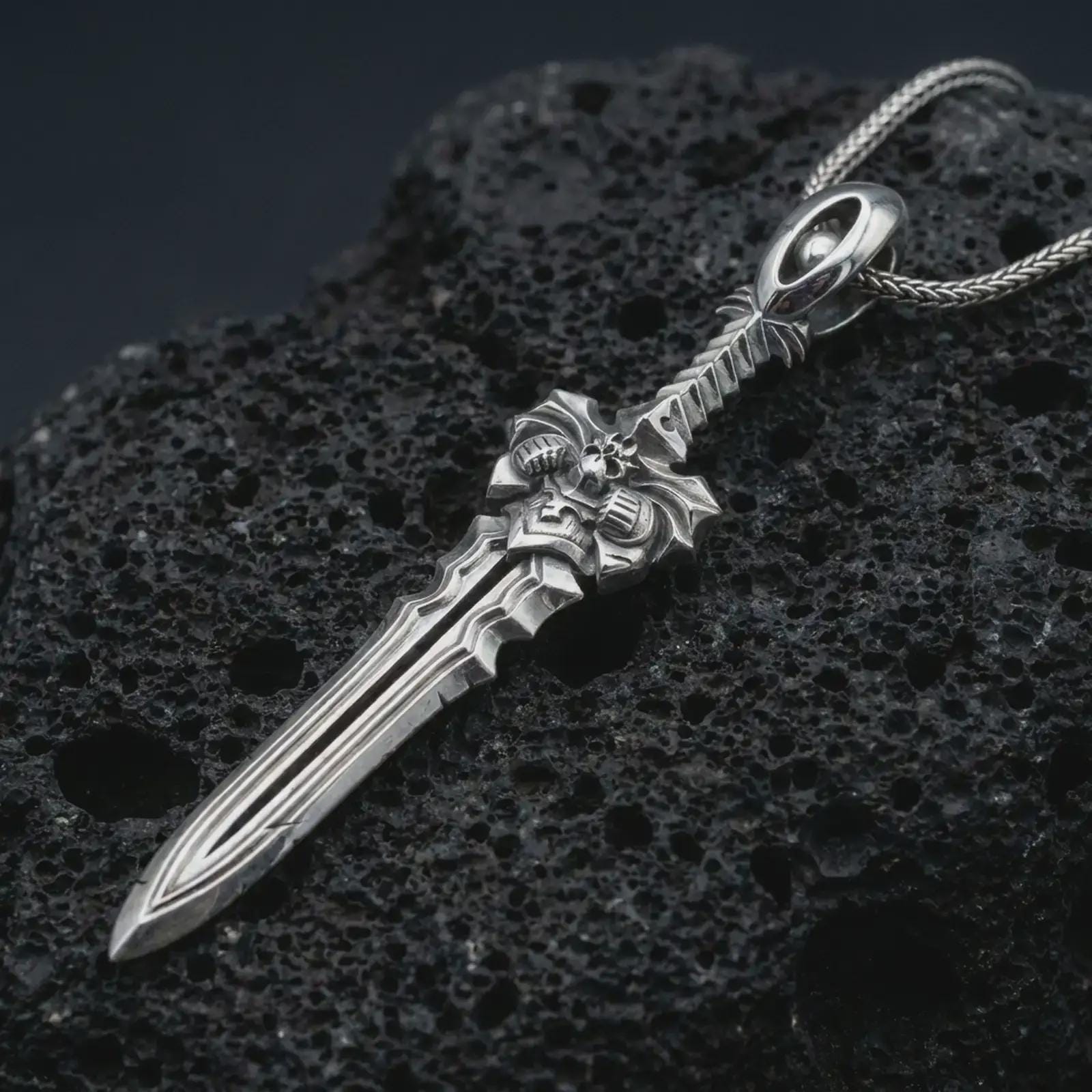 A polished silver fantasy sword pendant is displayed on black volcanic rock in a premium macro studio close-up with sharp blade lines and an ornate guard.