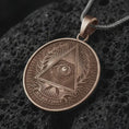 Load image into Gallery viewer, Bronze all-seeing eye pendant necklace on textured volcanic rock, close-up studio shot highlighting the triangle eye symbol, laurel wreath, radiant background, and antique silver contrast.
