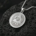 Load image into Gallery viewer, Polished silver all-seeing eye pendant necklace on textured volcanic rock, centered macro jewelry photo with detailed Illuminati-style engraving and bright silver highlights.
