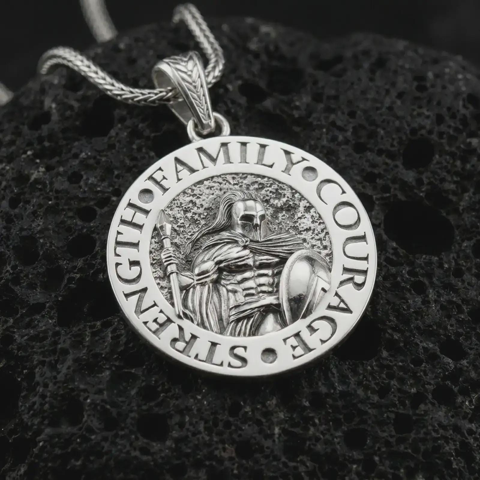 Polished silver Spartan warrior pendant necklace on textured volcanic rock, centered macro jewelry photo with detailed warrior armor, round medallion frame, and bright silver highlights.
