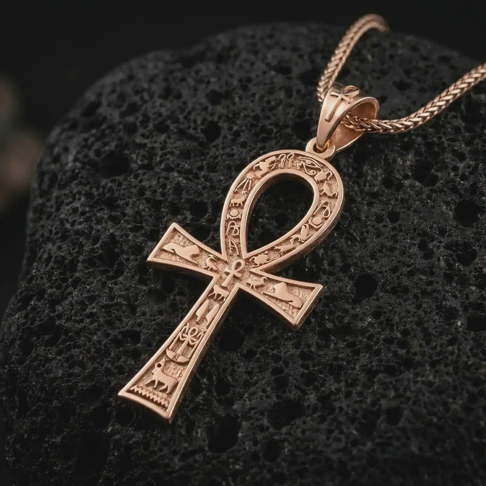Rose gold plated ankh cross pendant necklace on textured volcanic rock, detailed macro product shot with soft warm reflections and symbolic Egyptian styling.