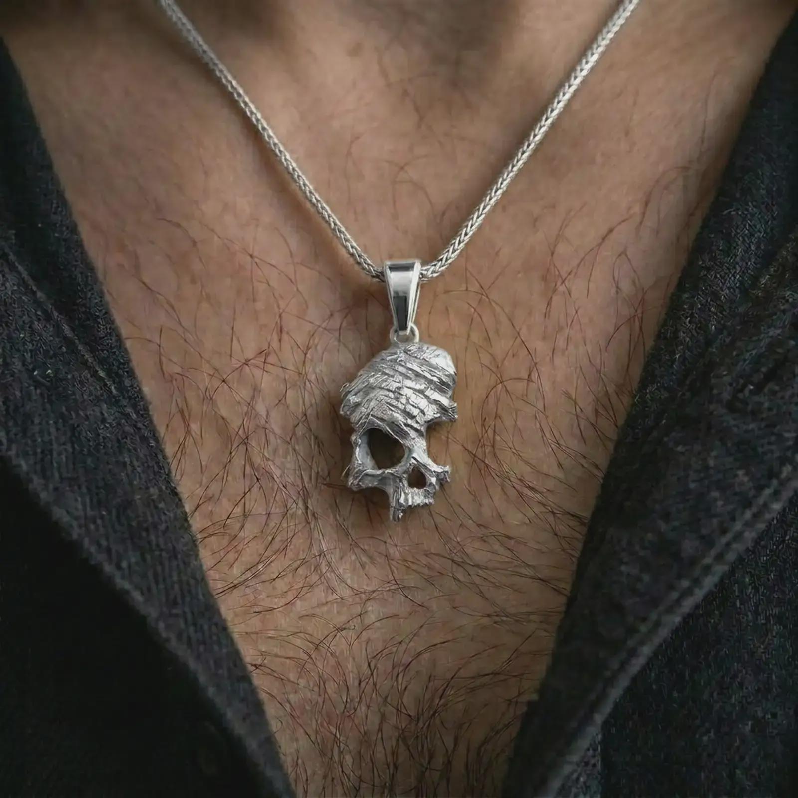 Polished silver cracked skull pendant necklace worn on the chest, masculine lifestyle shot highlighting the bright silver finish, fractured skull texture, and rugged sculptural detail.
