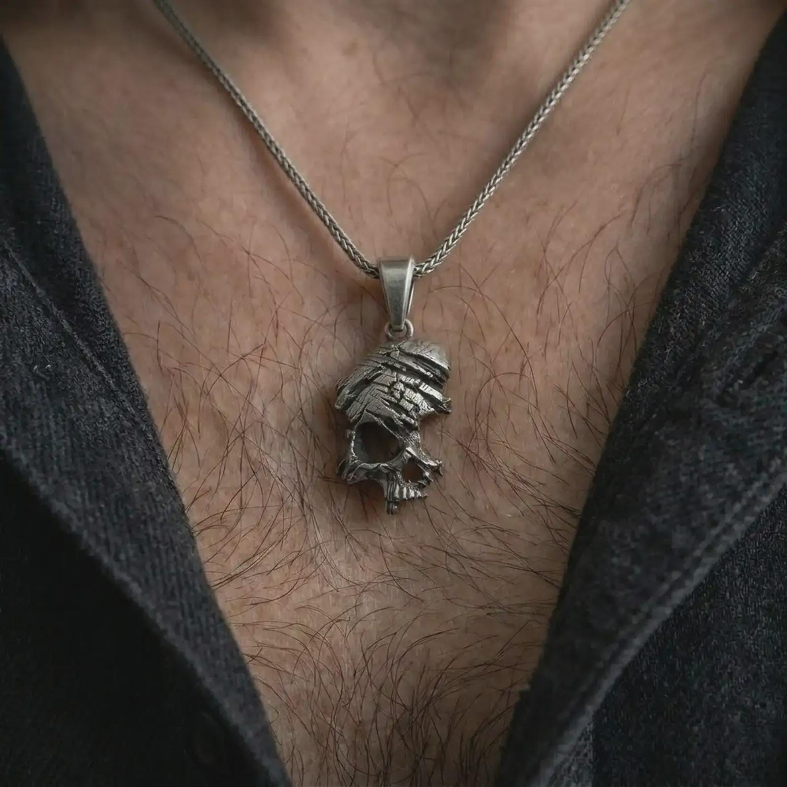 Oxidized cracked skull pendant necklace worn on the chest, close-up lifestyle jewelry photo showing the gothic skull charm on a spiga chain with dark clothing.