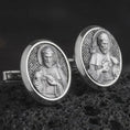 Load image into Gallery viewer, An oxidized Saint Francis cufflink pair rests on dark volcanic rock in a macro studio close-up, showing a detailed Catholic saint relief inside oval frames.
