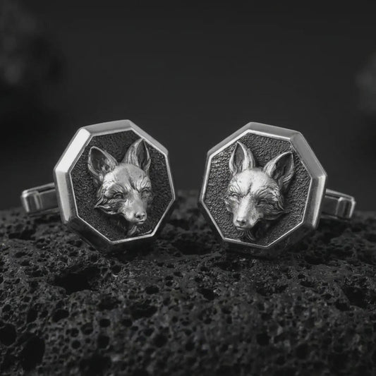 An oxidized fox head cufflink pair rests on dark volcanic rock in a macro studio close-up, showing sculpted woodland animal detail inside octagon frames.