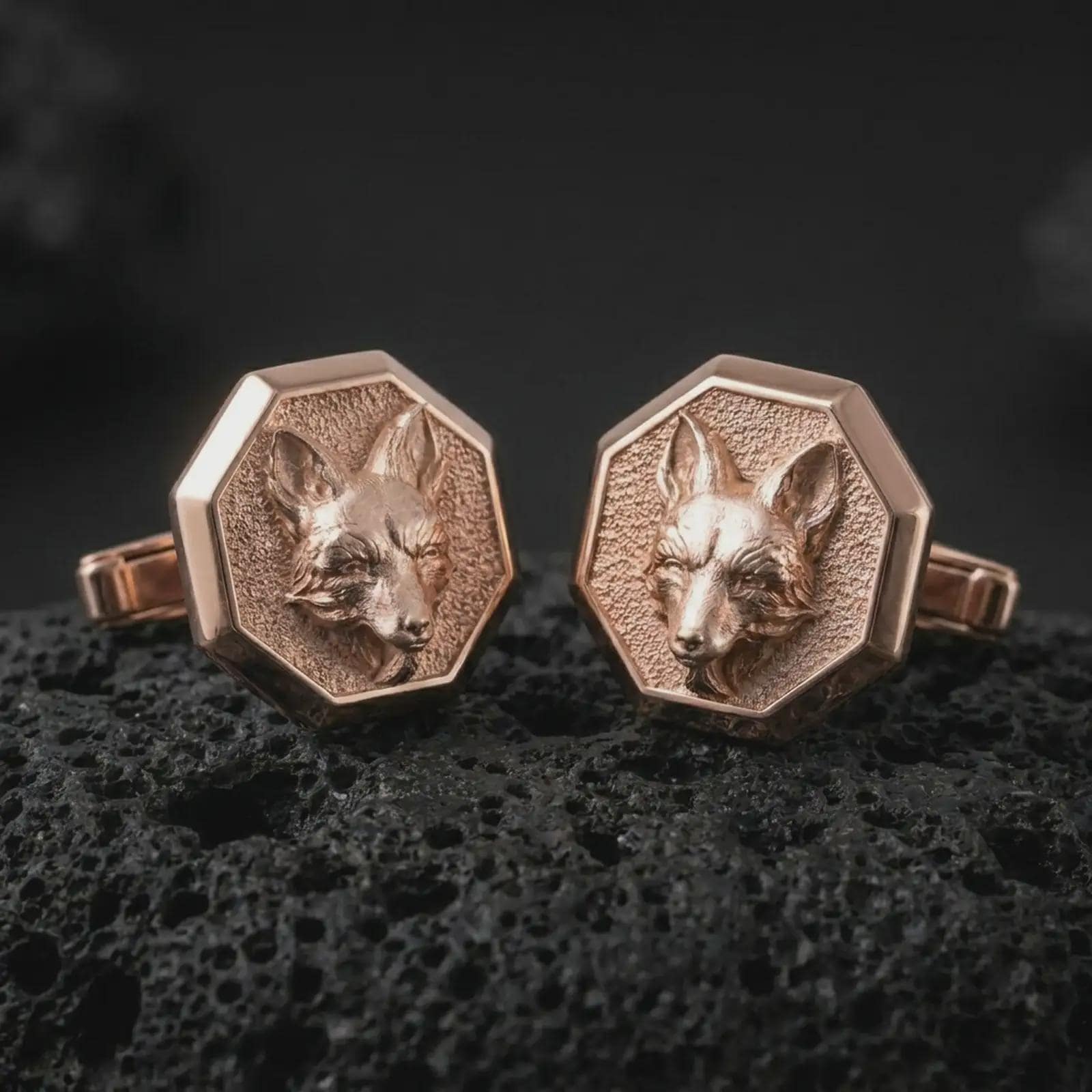 Rose gold plated fox head cufflinks are photographed on porous volcanic rock in a close-up studio composition with refined luxury lighting and detailed fox features.