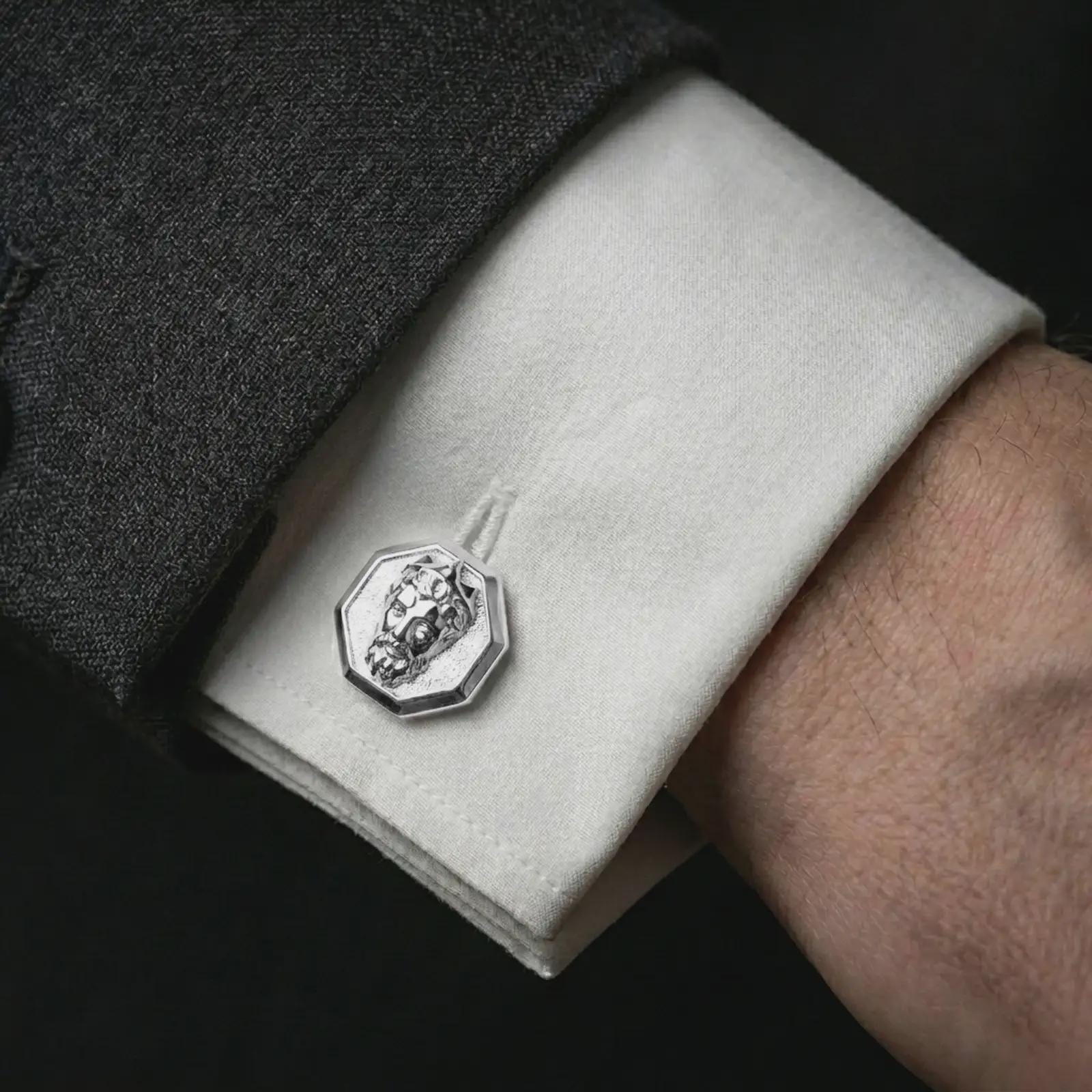 A polished silver Zeus cufflink is worn on a shirt cuff in a premium close-up lifestyle image, showing the sculpted Greek god face clearly.