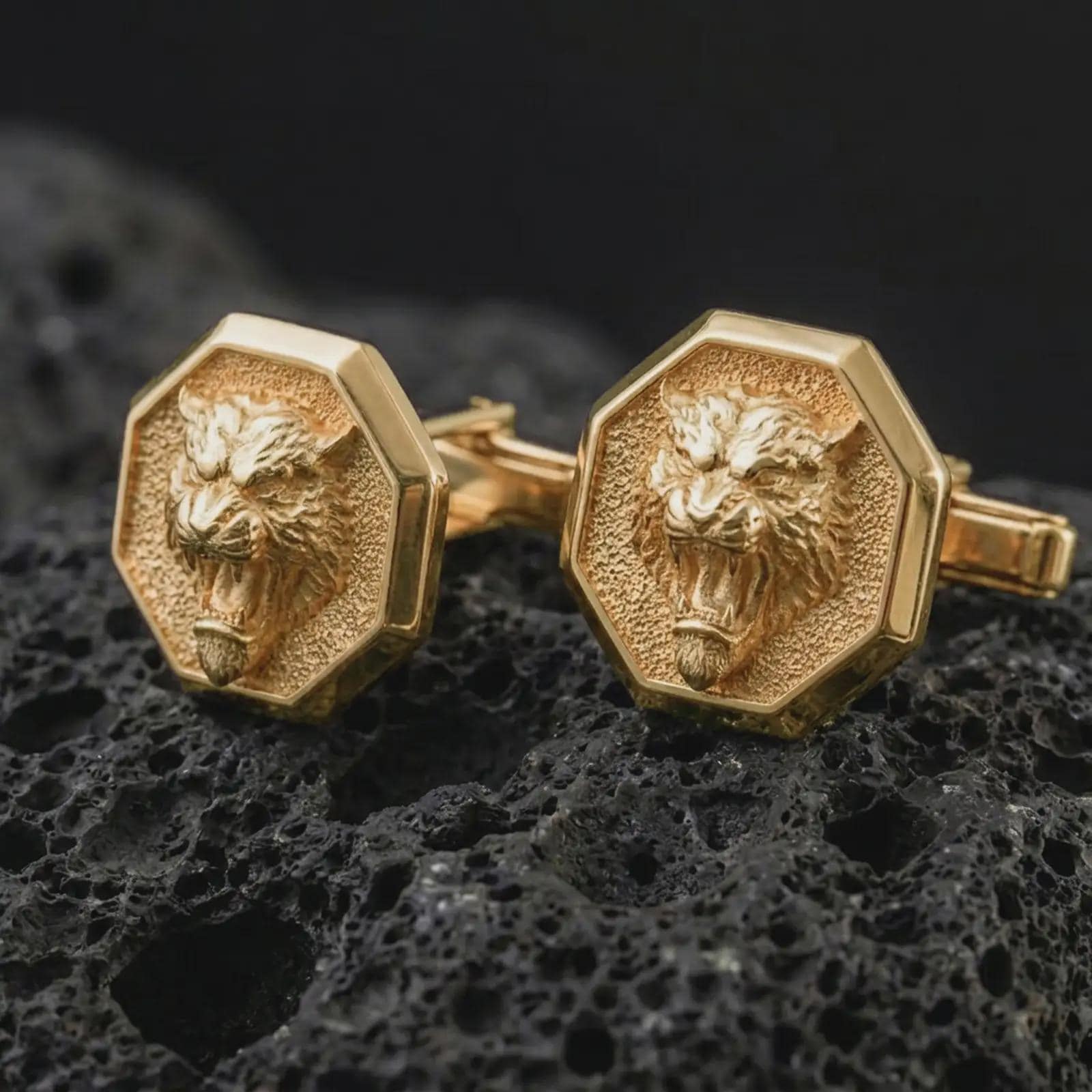 Gold plated tiger head cufflinks sit on textured volcanic rock in a dramatic studio macro shot, highlighting the powerful animal motif and formal accessory design.