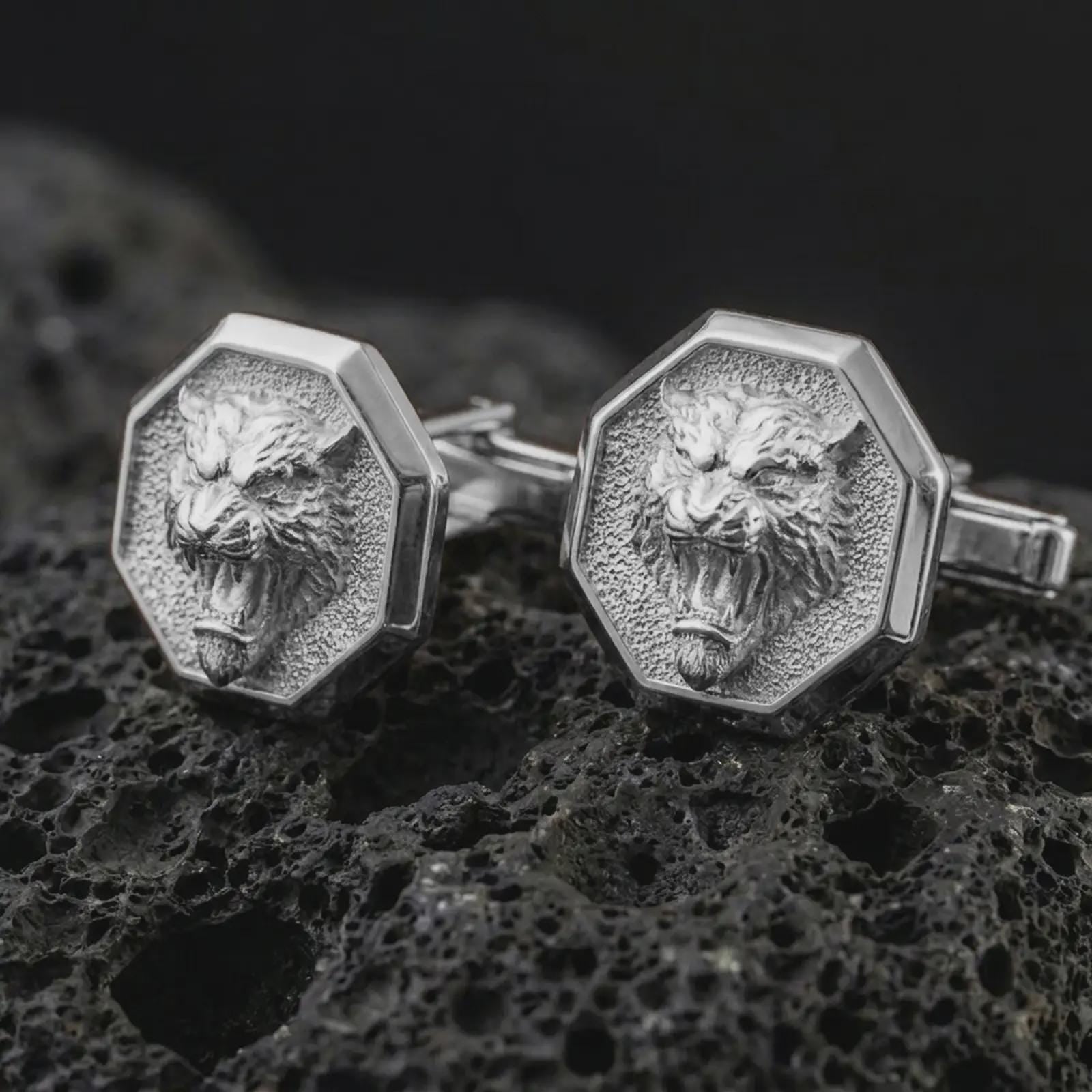 Polished silver tiger head cufflinks are displayed on black volcanic rock in a premium macro studio close-up with sharp facial texture and clean geometric edges.