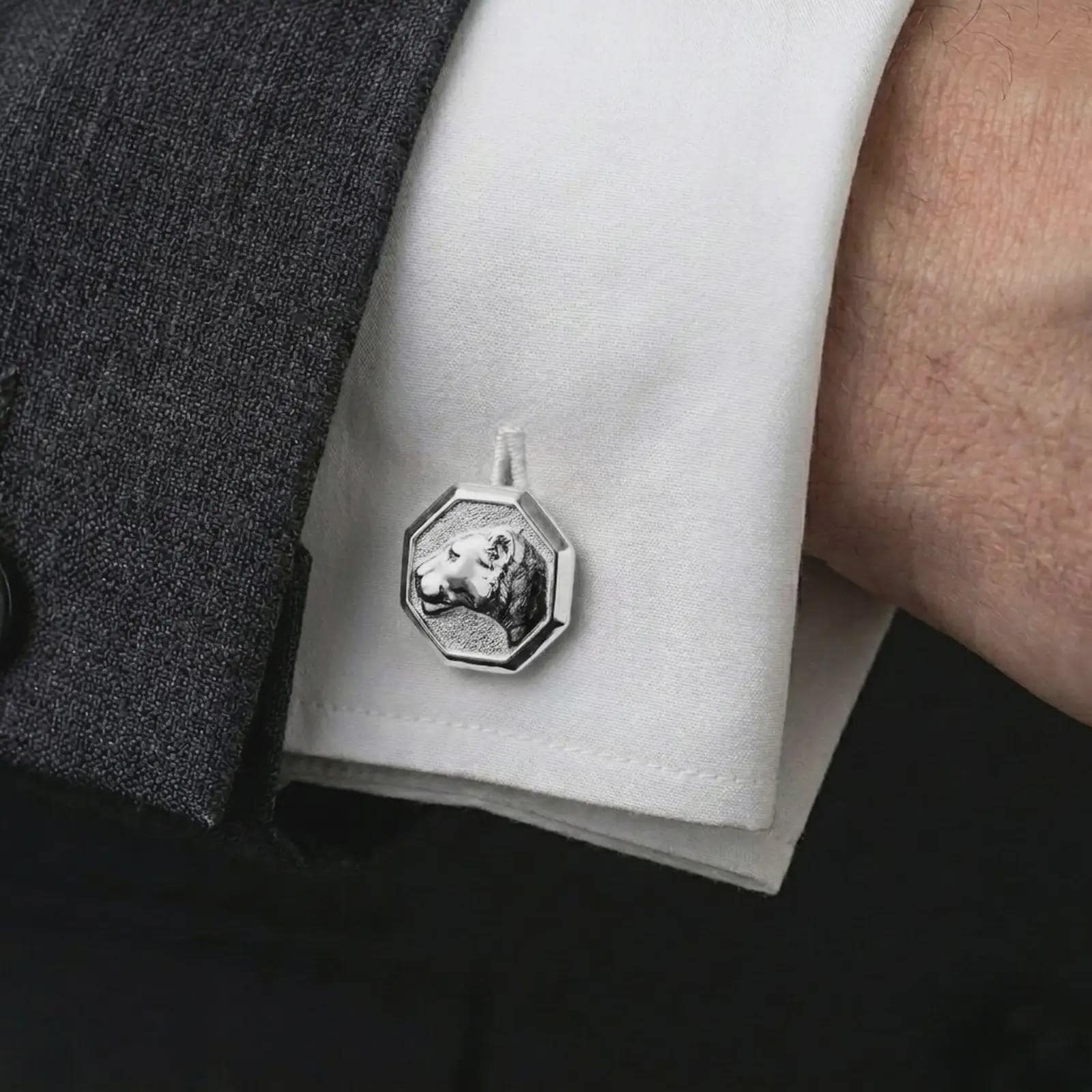 A polished silver lioness head cufflink is worn on a shirt cuff in a premium close-up lifestyle image, showing the sculpted lioness profile clearly.