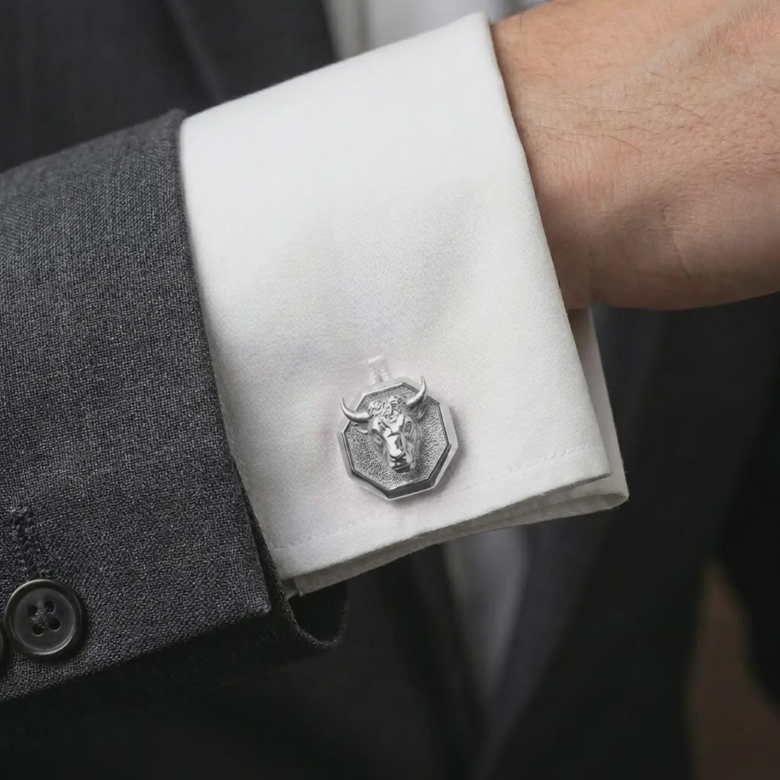A polished silver bull head cufflink is worn on a shirt cuff in a premium close-up lifestyle image, showing the sculpted horned bull face clearly.
