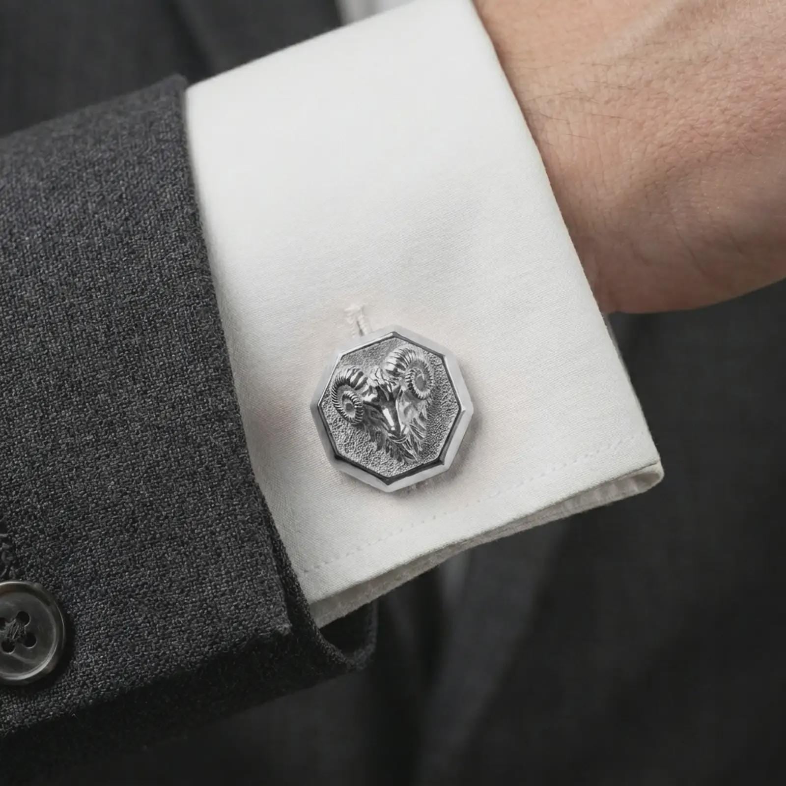 A polished silver ram head cufflink is worn on a shirt cuff in a premium close-up lifestyle image, showing the sculpted curled horn ram face clearly.