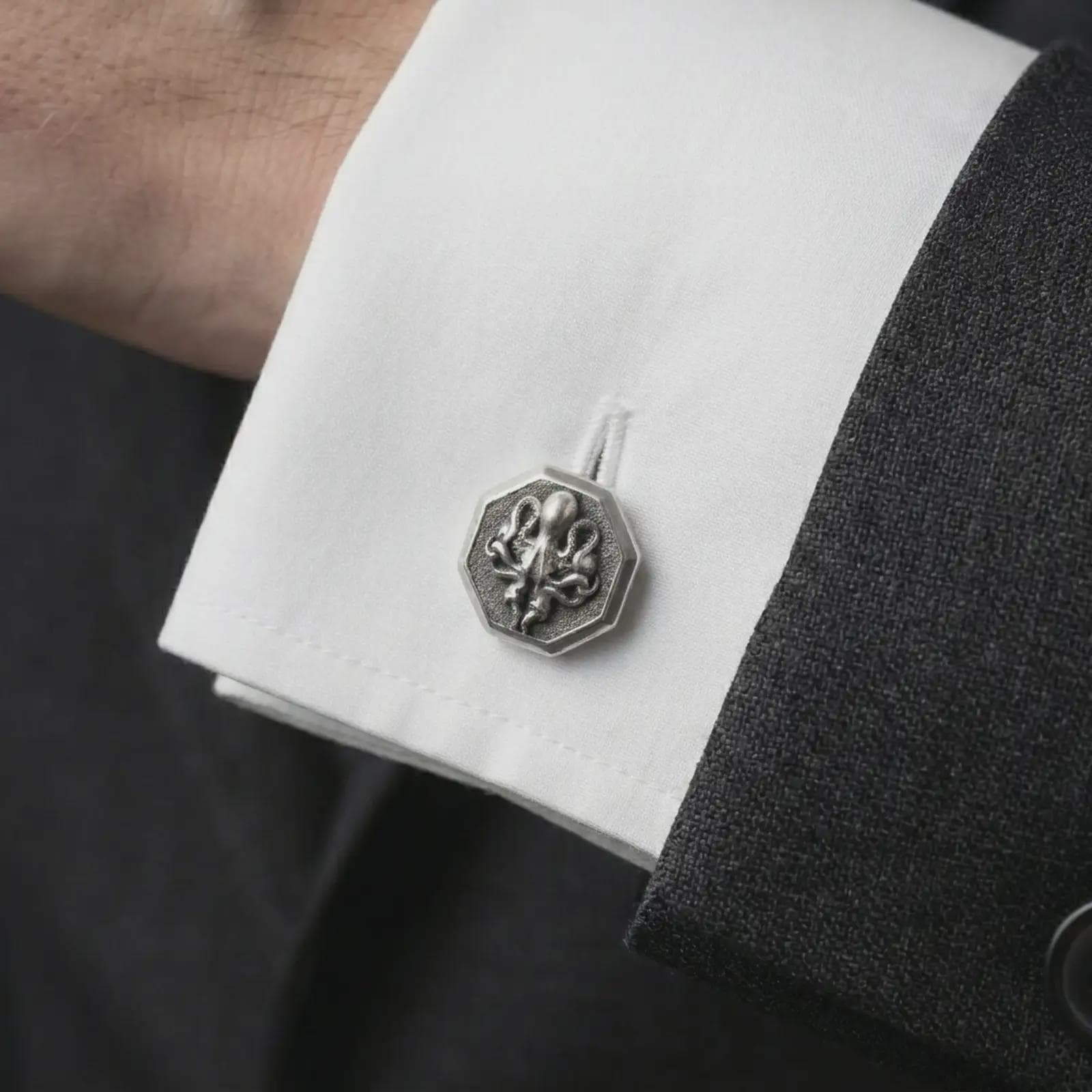 An oxidized octopus cufflink is worn on a white shirt cuff in a close-up lifestyle shot, styled with a dark suit for a bold nautical look.