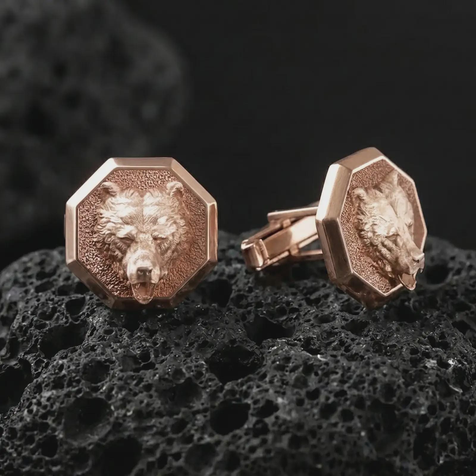 Rose gold plated bear head cufflinks are photographed on porous volcanic rock in a close-up studio composition with refined luxury lighting and detailed bear features.