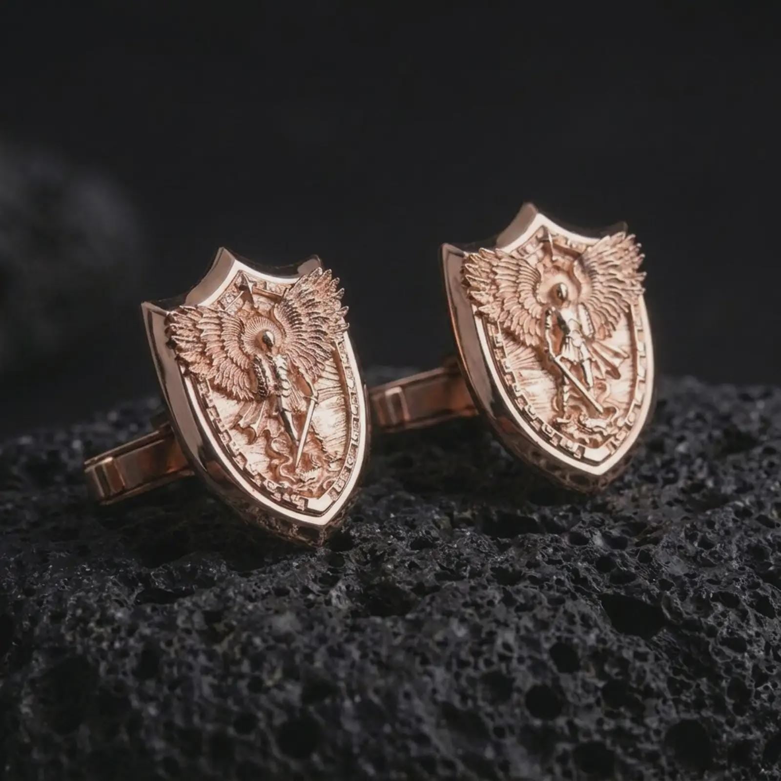 Rose gold plated Saint Michael cufflinks are photographed on porous volcanic rock in a close-up studio composition with refined luxury lighting and religious detail.