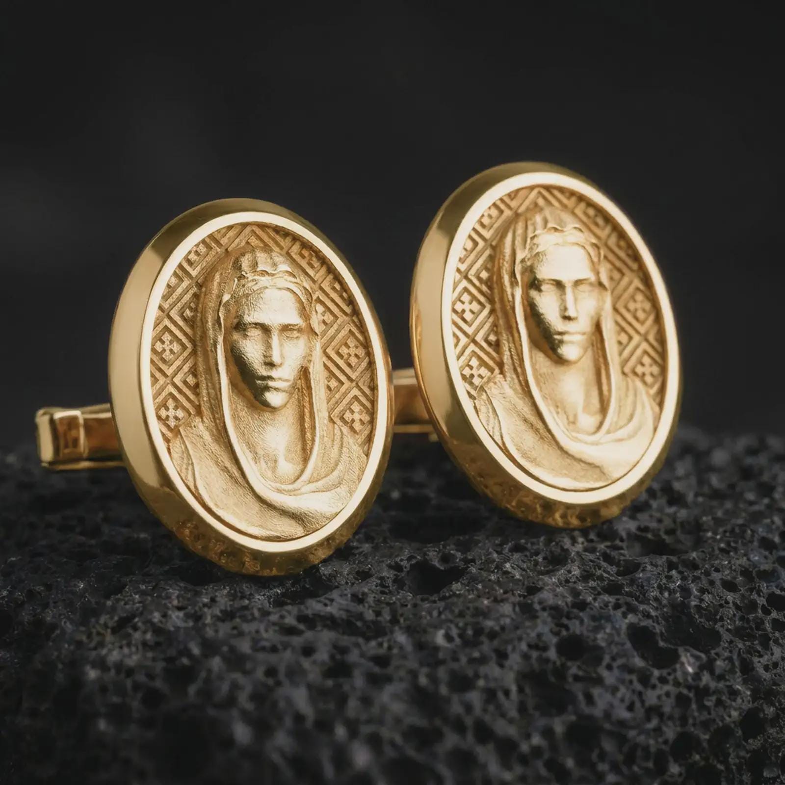 Gold plated Virgin Mary cufflinks sit on textured volcanic rock in a dramatic studio macro shot, highlighting the sacred Marian portrait design.