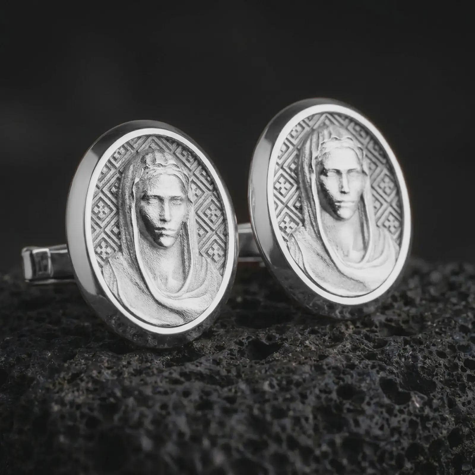 Polished silver Virgin Mary cufflinks are displayed on black volcanic rock in a premium macro studio close-up with detailed Catholic devotional artwork.