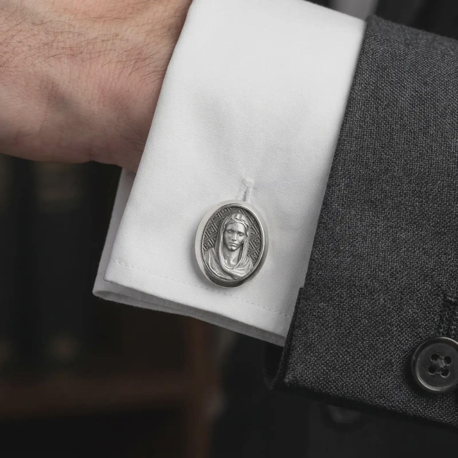 An oxidized Virgin Mary cufflink is worn on a white shirt cuff in a close-up lifestyle shot, styled with a dark suit as a meaningful Catholic accessory.