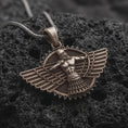 Load image into Gallery viewer, A bronze Faravahar pendant rests on dark volcanic rock in a macro studio close-up, showing a detailed winged Persian symbol with a central figure.
