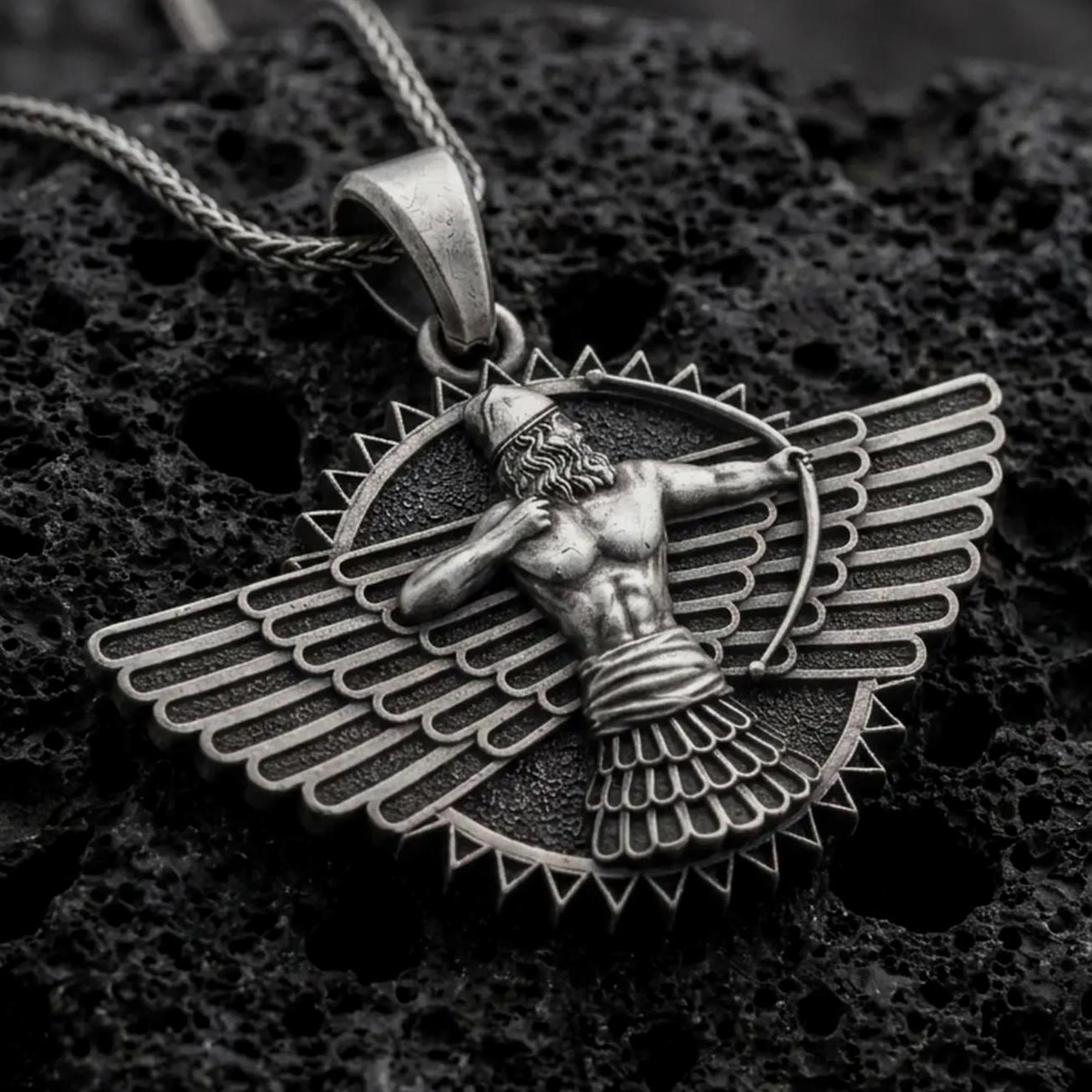 An oxidized Faravahar pendant rests on dark volcanic rock in a macro studio close-up, showing a detailed winged Persian symbol with a central figure.