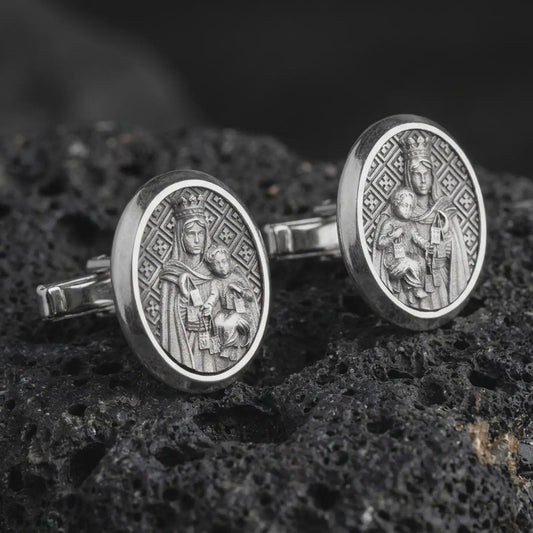 An oxidized Blessed Mother cufflink pair rests on dark volcanic rock in a macro studio close-up, showing the Virgin Mary and Child relief in oval frames.
