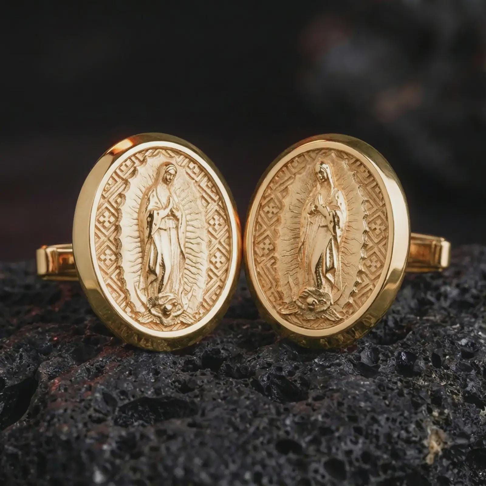 Gold plated Our Lady of Guadalupe cufflinks sit on textured volcanic rock in a dramatic studio macro shot, highlighting the sacred Virgin Mary design.
