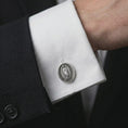 Load image into Gallery viewer, An oxidized Our Lady of Guadalupe cufflink is worn on a white shirt cuff in a close-up lifestyle shot, styled with a dark suit as a meaningful Catholic accessory.
