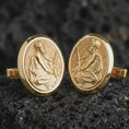 Load image into Gallery viewer, Gold plated Pensive Christ cufflinks sit on textured volcanic rock in a dramatic studio macro shot, highlighting the sacred Jesus medallion design.
