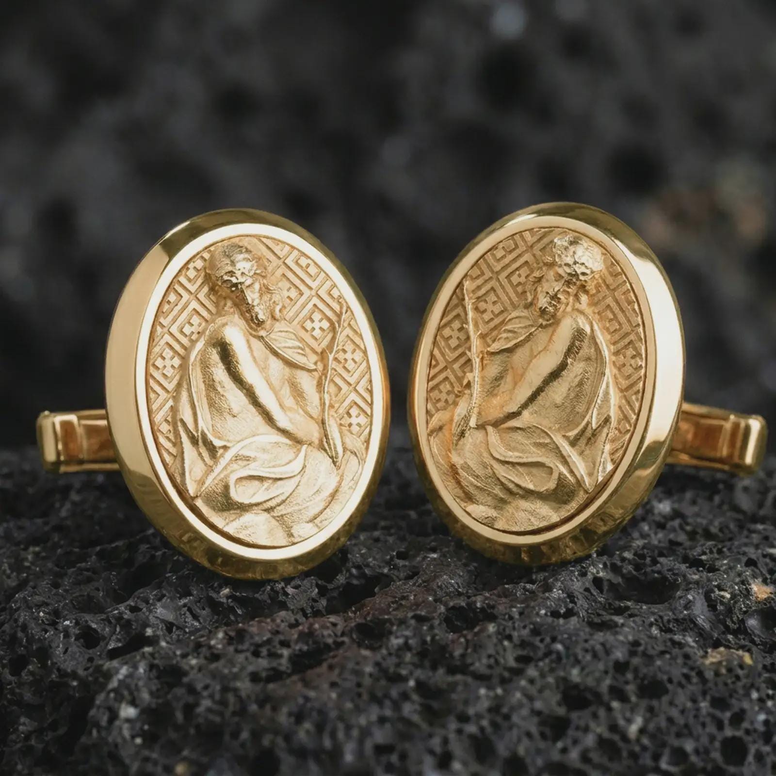 Gold plated Pensive Christ cufflinks sit on textured volcanic rock in a dramatic studio macro shot, highlighting the sacred Jesus medallion design.