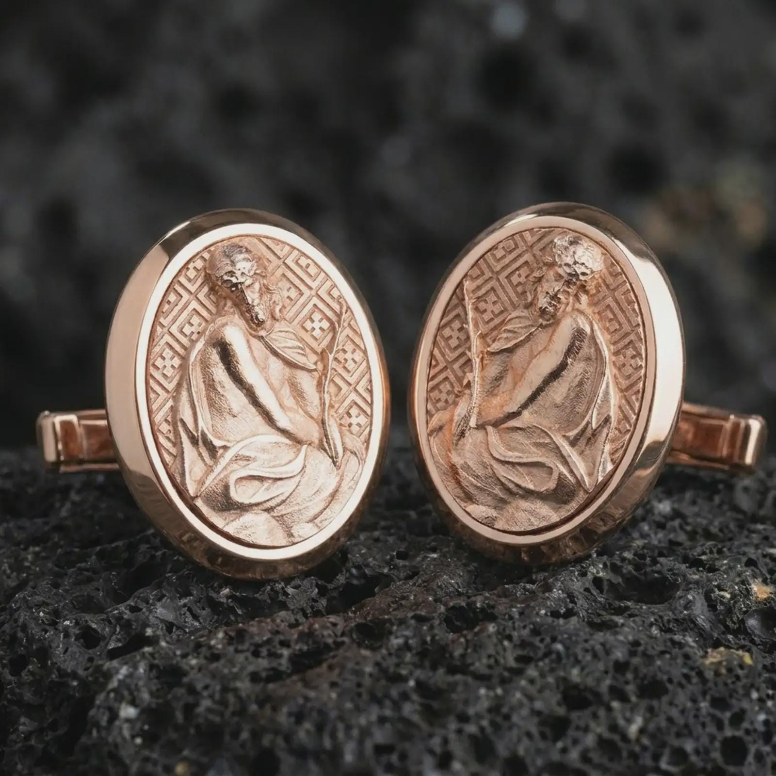 Rose gold plated Pensive Christ cufflinks are photographed on porous volcanic rock in a close-up studio composition with refined luxury lighting and religious detail.