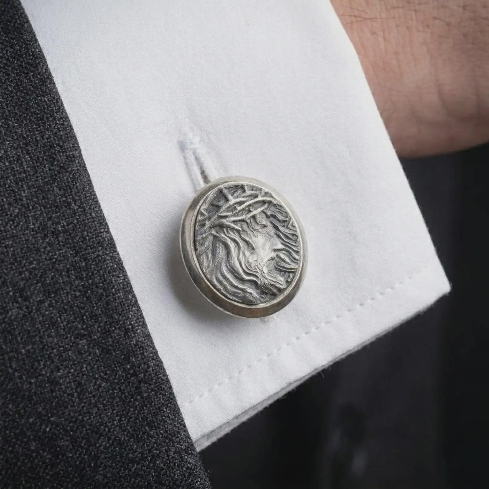 An oxidized Jesus Crown of Thorns cufflink is worn on a white shirt cuff in a close-up lifestyle shot, styled with a dark suit as a meaningful Christian accessory.