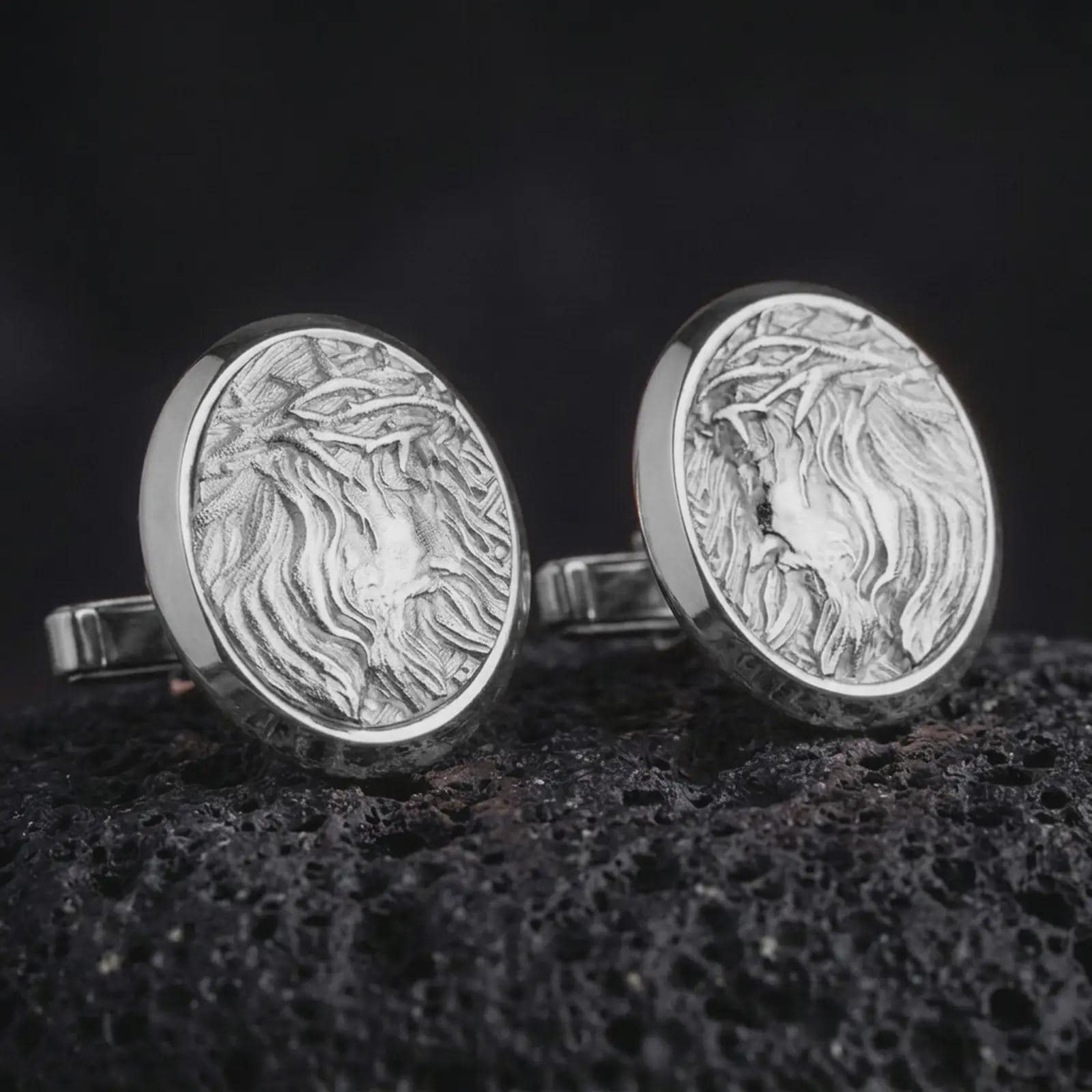 Polished silver Jesus Crown of Thorns cufflinks are displayed on black volcanic rock in a premium macro studio close-up with detailed Christian devotional artwork.