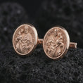 Load image into Gallery viewer, Rose gold plated Saint Joseph cufflinks presented on volcanic rock in a dramatic macro studio image, showcasing intricate Catholic craftsmanship and devotional artwork.
