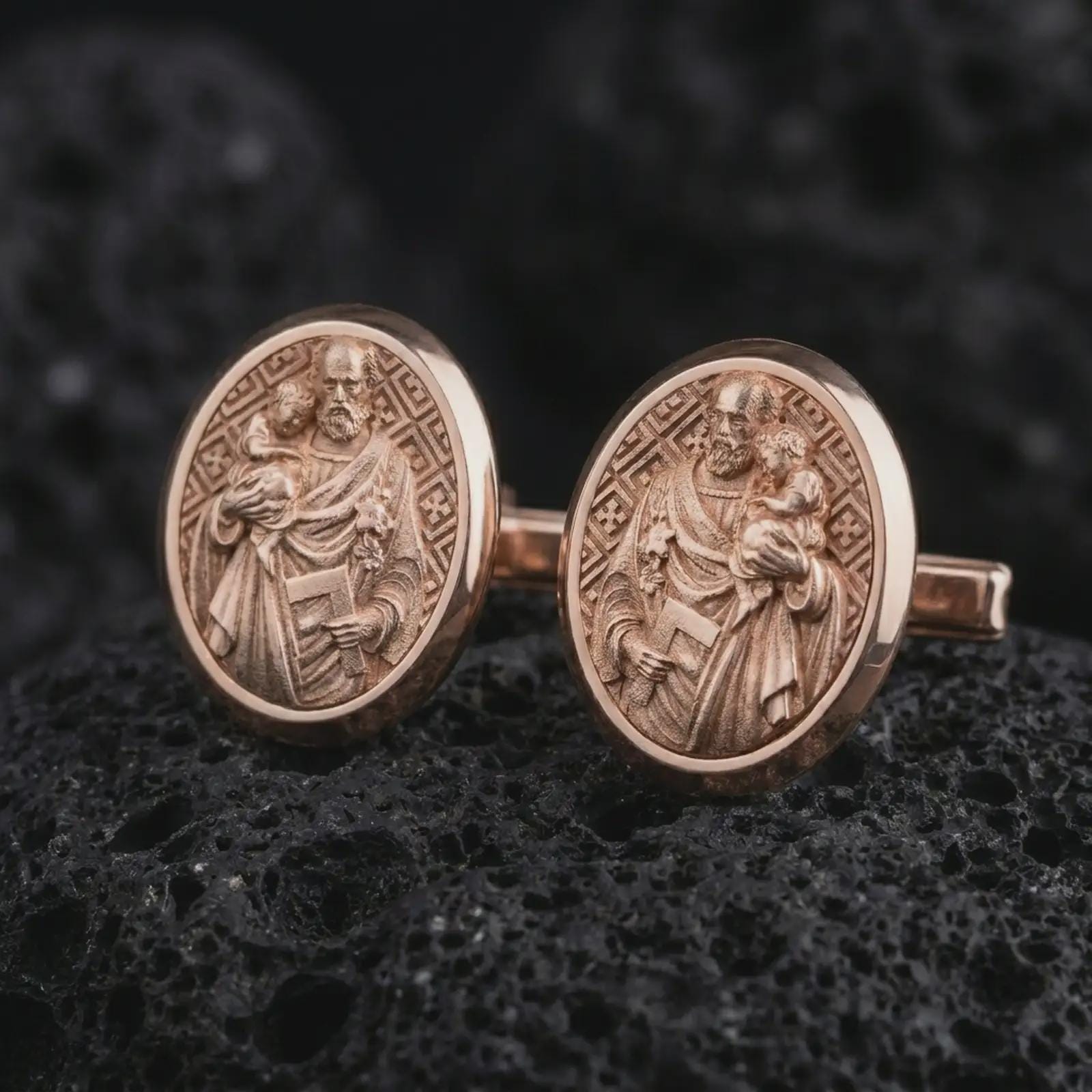 Rose gold plated Saint Joseph cufflinks presented on volcanic rock in a dramatic macro studio image, showcasing intricate Catholic craftsmanship and devotional artwork.