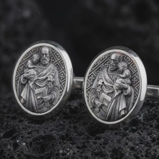 Oxidized Saint Joseph cufflinks displayed on dark volcanic rock in a macro studio photograph, featuring Saint Joseph holding the Christ Child with finely engraved Christian details.