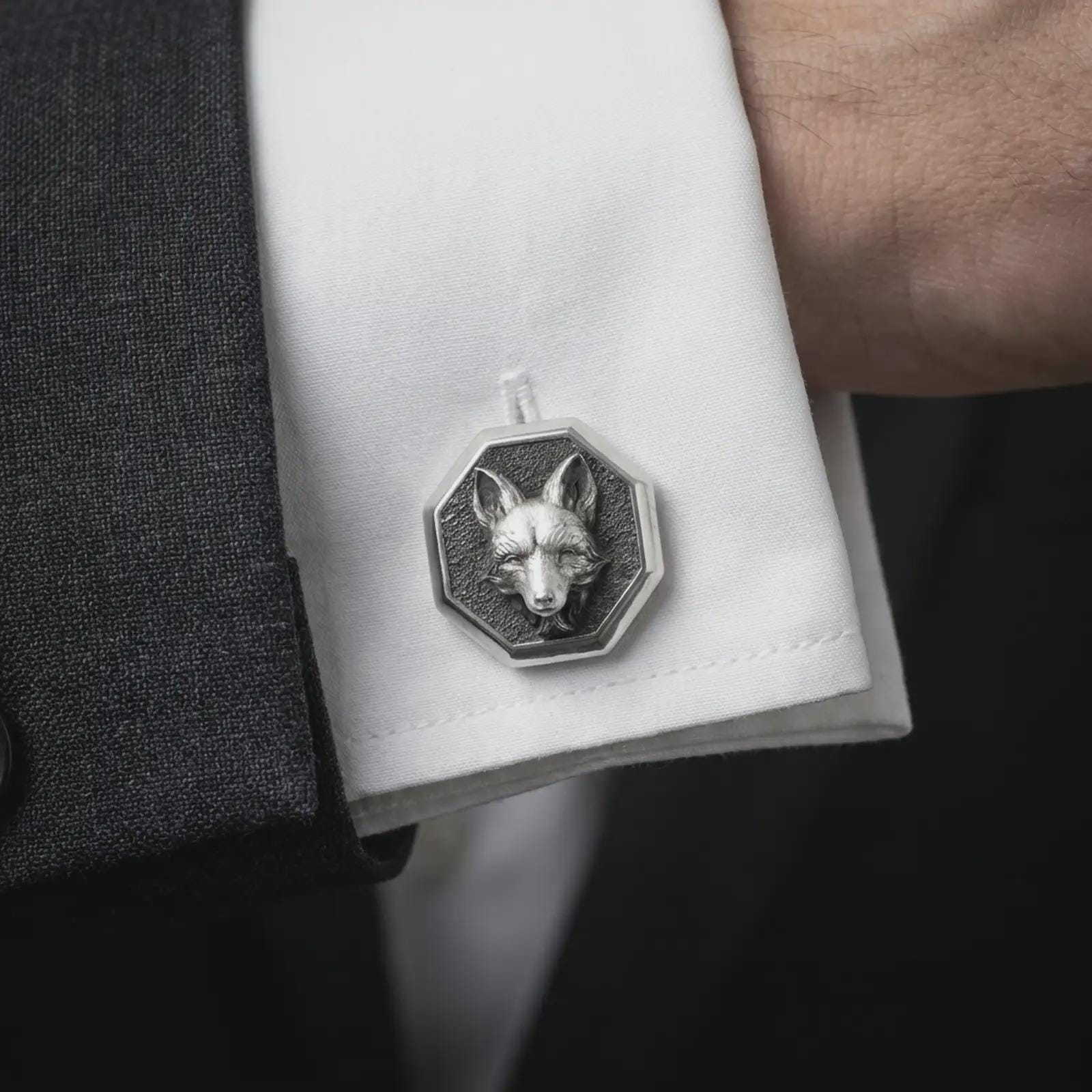 An oxidized fox head cufflink is worn on a white shirt cuff in a close-up lifestyle shot, styled with a dark suit for a refined woodland-inspired look.
