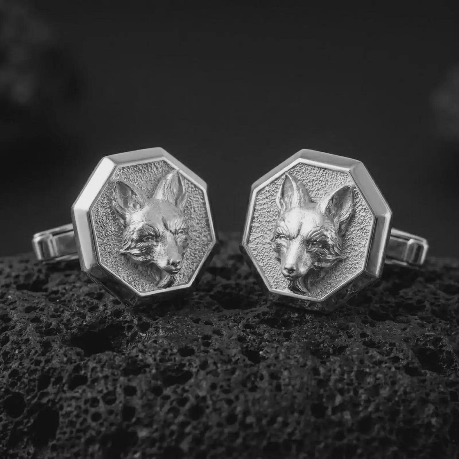 Polished silver fox head cufflinks are displayed on black volcanic rock in a premium macro studio close-up with sharp facial texture and clean geometric edges.