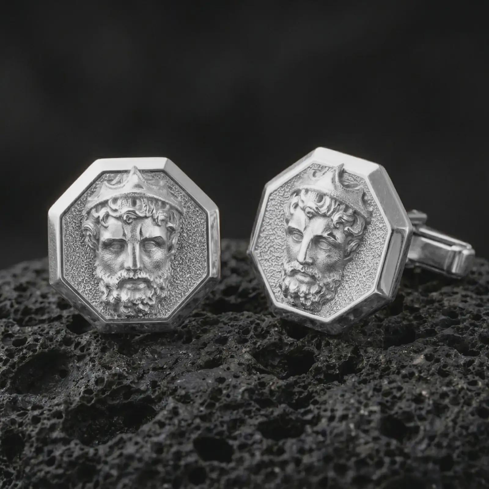 Polished silver Zeus cufflinks are displayed on black volcanic rock in a premium macro studio close-up with sharp facial texture and clean geometric edges.