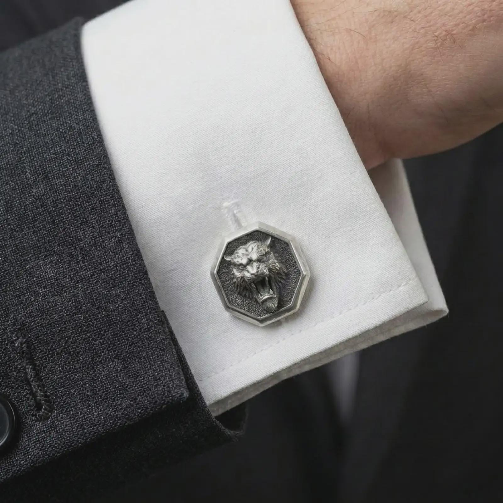 An oxidized tiger head cufflink is worn on a white shirt cuff in a close-up lifestyle shot, styled with a dark suit for a bold formal look.